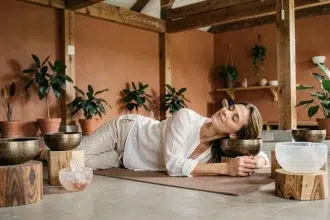 Femme allongée sur un tapis de yoga entourée de bols tibétains lors d'un bain sonore dans un studio de bien-être