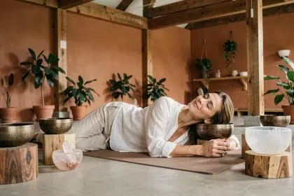Femme allongée sur un tapis de yoga entourée de bols tibétains lors d'un bain sonore dans un studio de bien-être