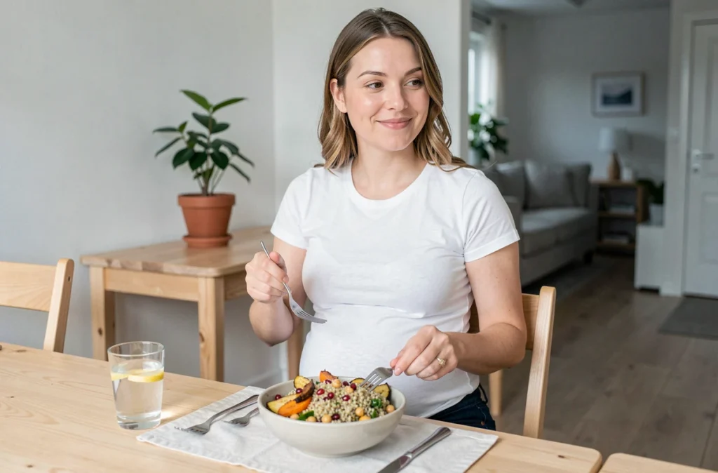 Femme enceinte assise à table savourant un repas sain à base de quinoa et légumes rôtis dans un intérieur scandinave